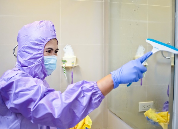 A cleaner waering PPE cleaning a mirror in a bathroom