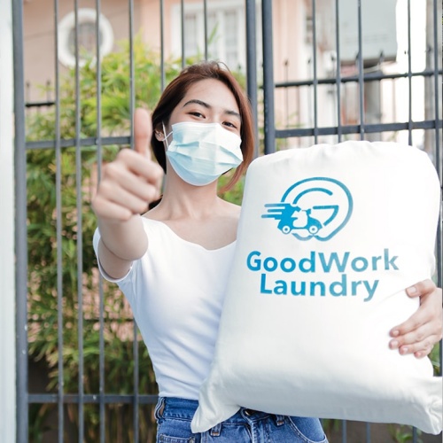 Woman wearing facemask, holding bag of laundry, giving a thumbs up